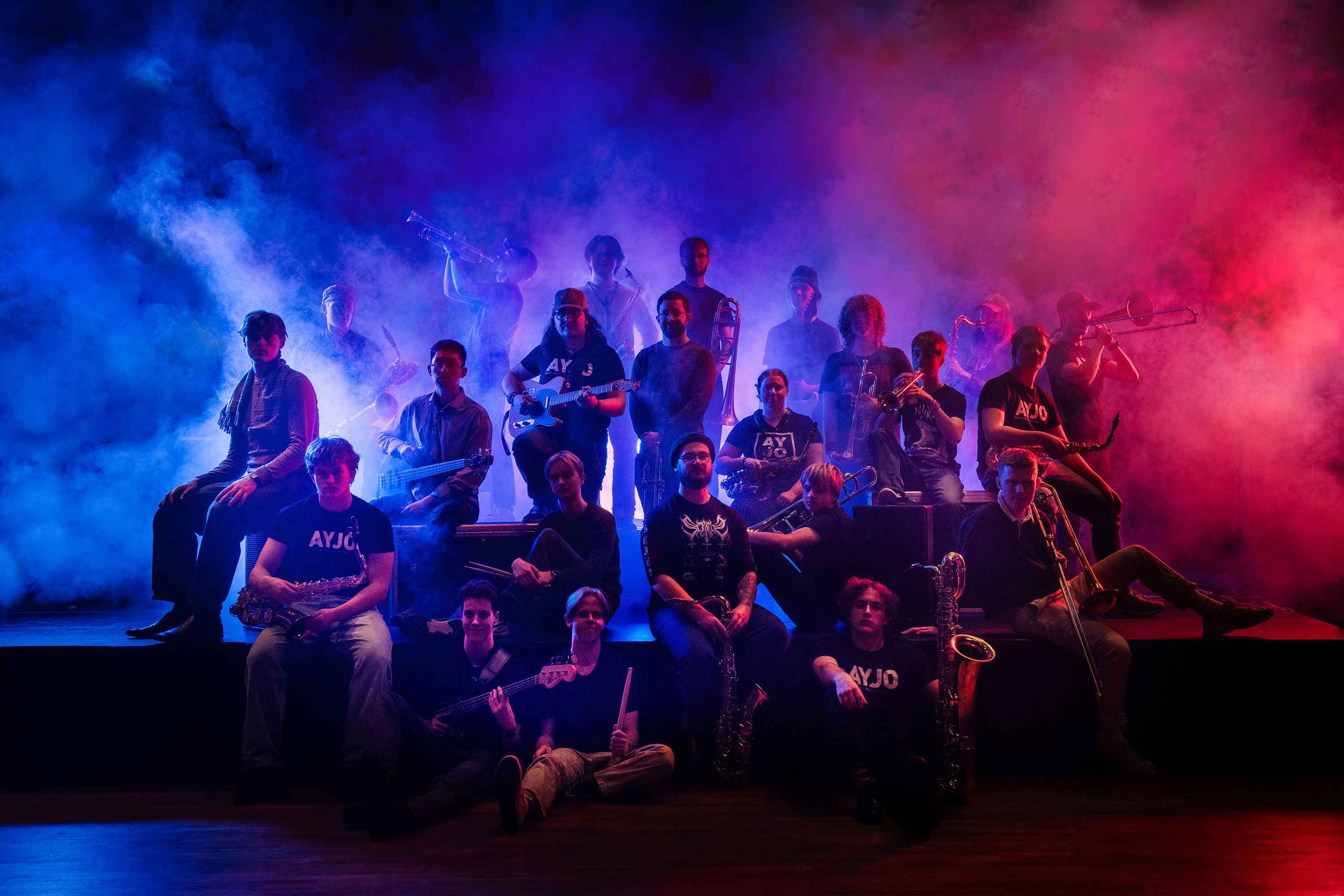 Deltagarna i AYJO står uppställda med instrument i en mörk lokal fylld av rök som lyses upp med ett rött och blått ljus. 