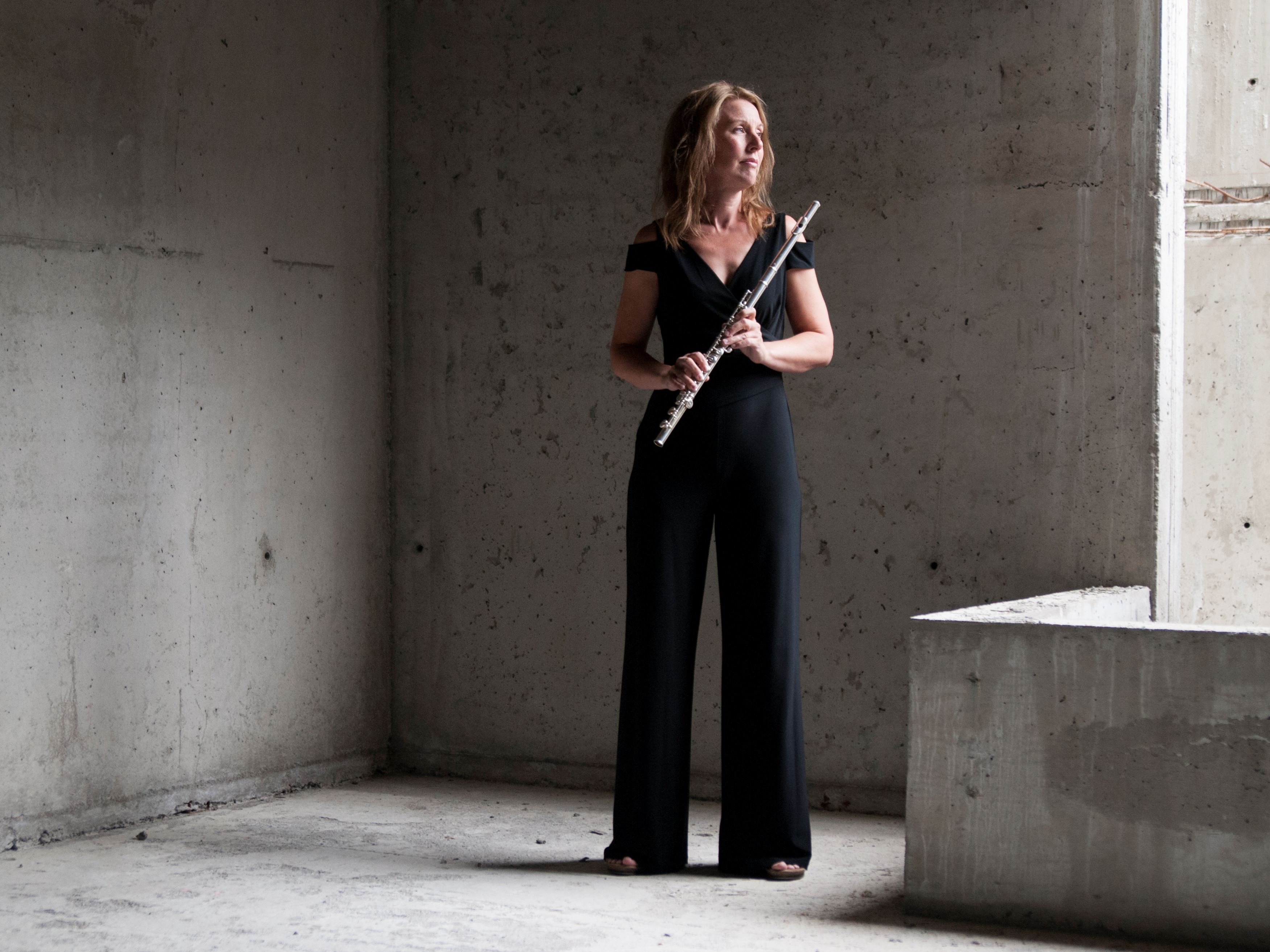 Helbild av flöjtisten Sara Hammarström som står i en betongmiljö med ett musi...