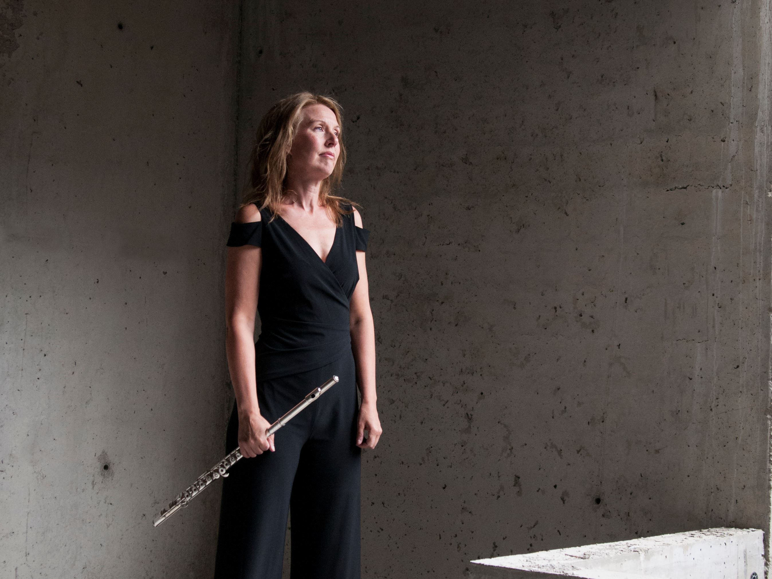 Helbild av flöjtisten Sara Hammarström som står i en betongmiljö med ett musi...