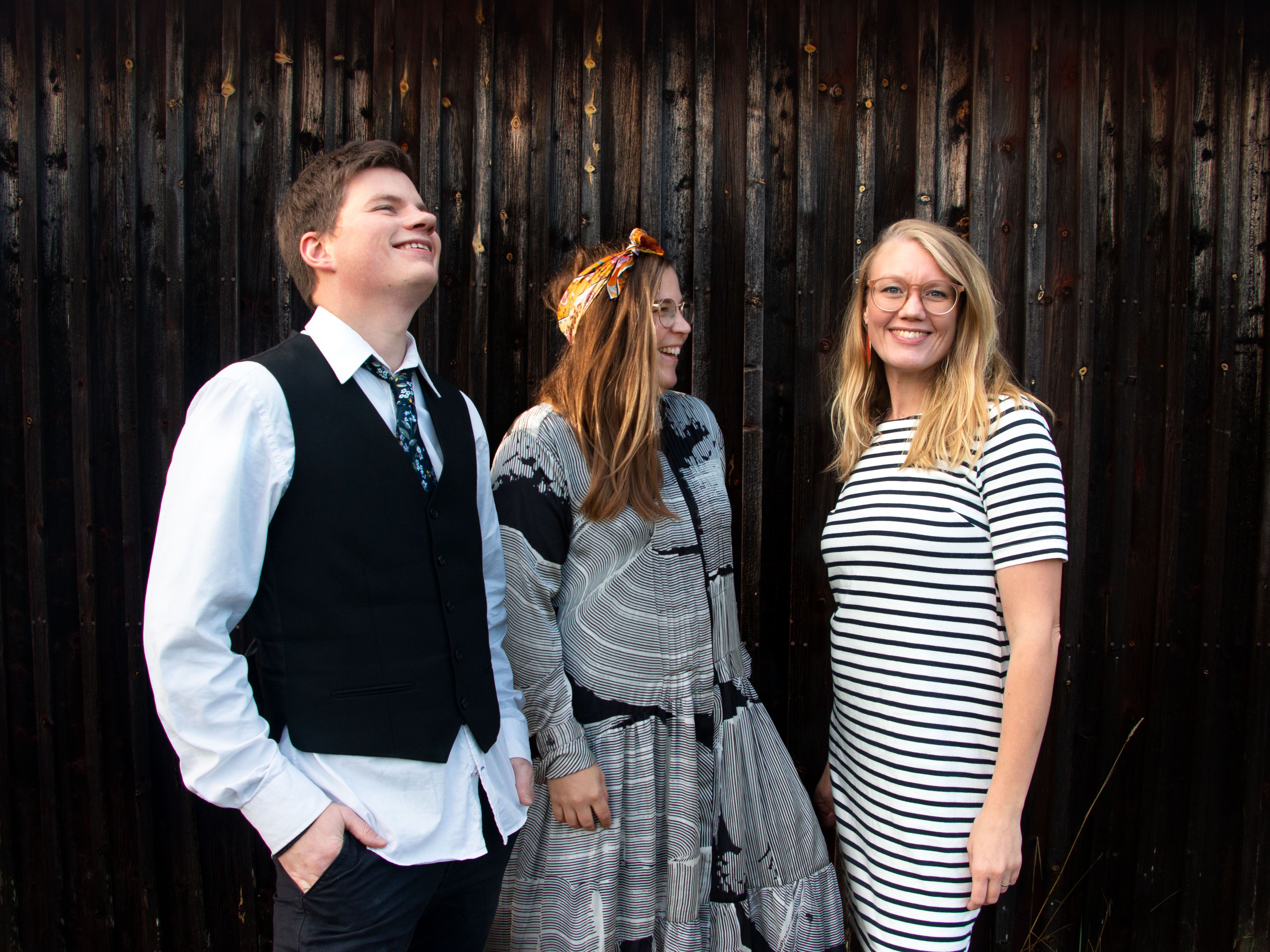 En bild med de tre medlemmarna i The Chickpeas band stående vid en trävägg