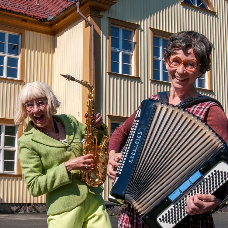 Rollfigurerna Ann-Gerd och Gullan står med sina instrument utanför en skola