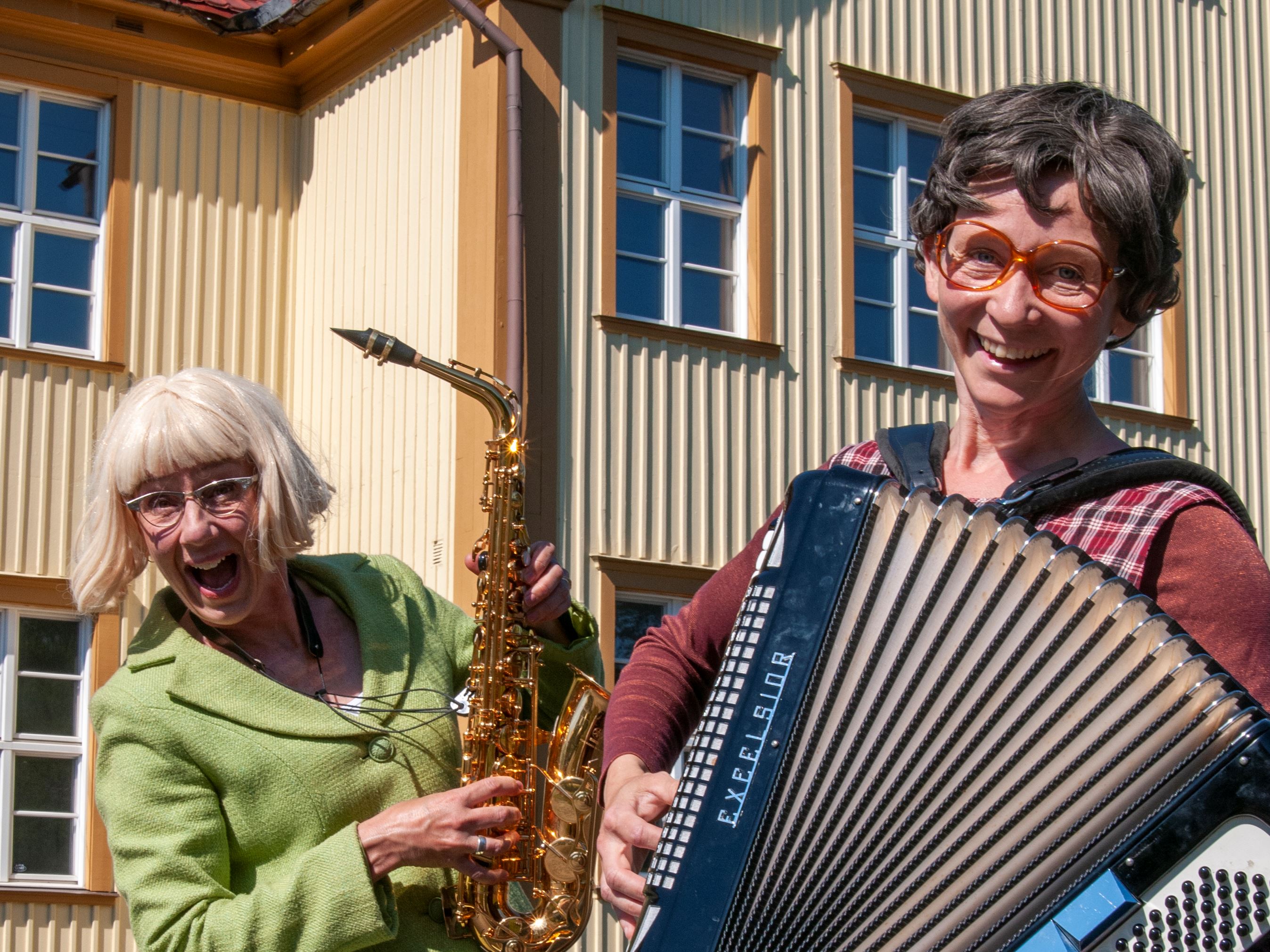 Rollfigurerna Ann-Gerd och Gullan står med sina instrument utanför en skola