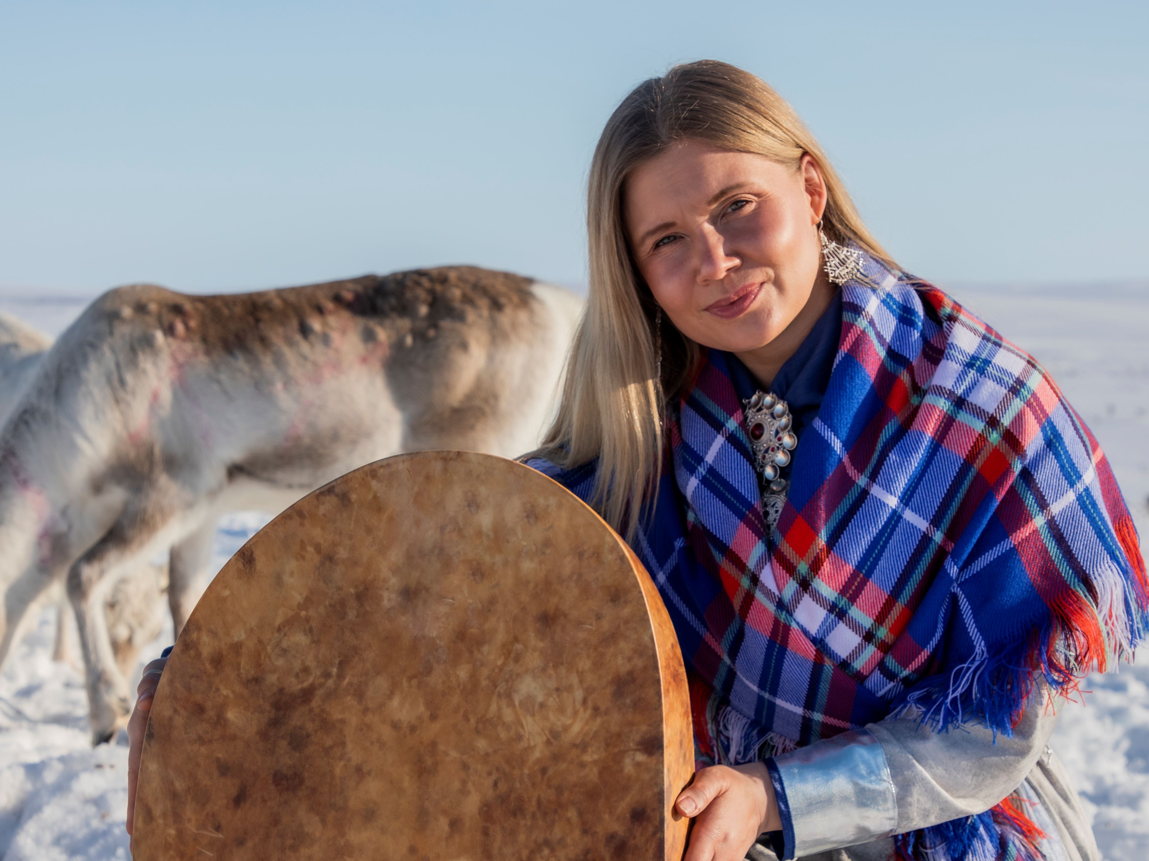 Artisten Ingá-Máret Gaup-Juuso sitter i ett vinterlandskap med renar i bakgrunden