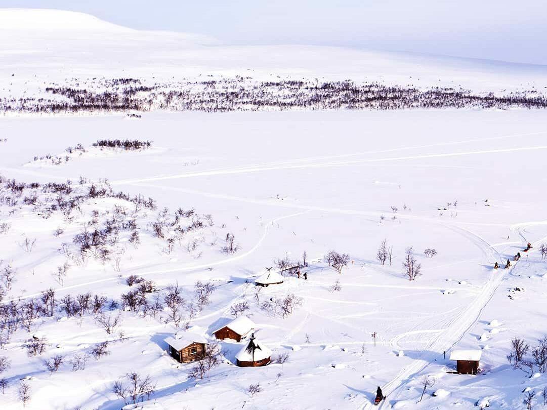 En panoramabild över ett vinterlandskap med några stugor och träd i förgrunden