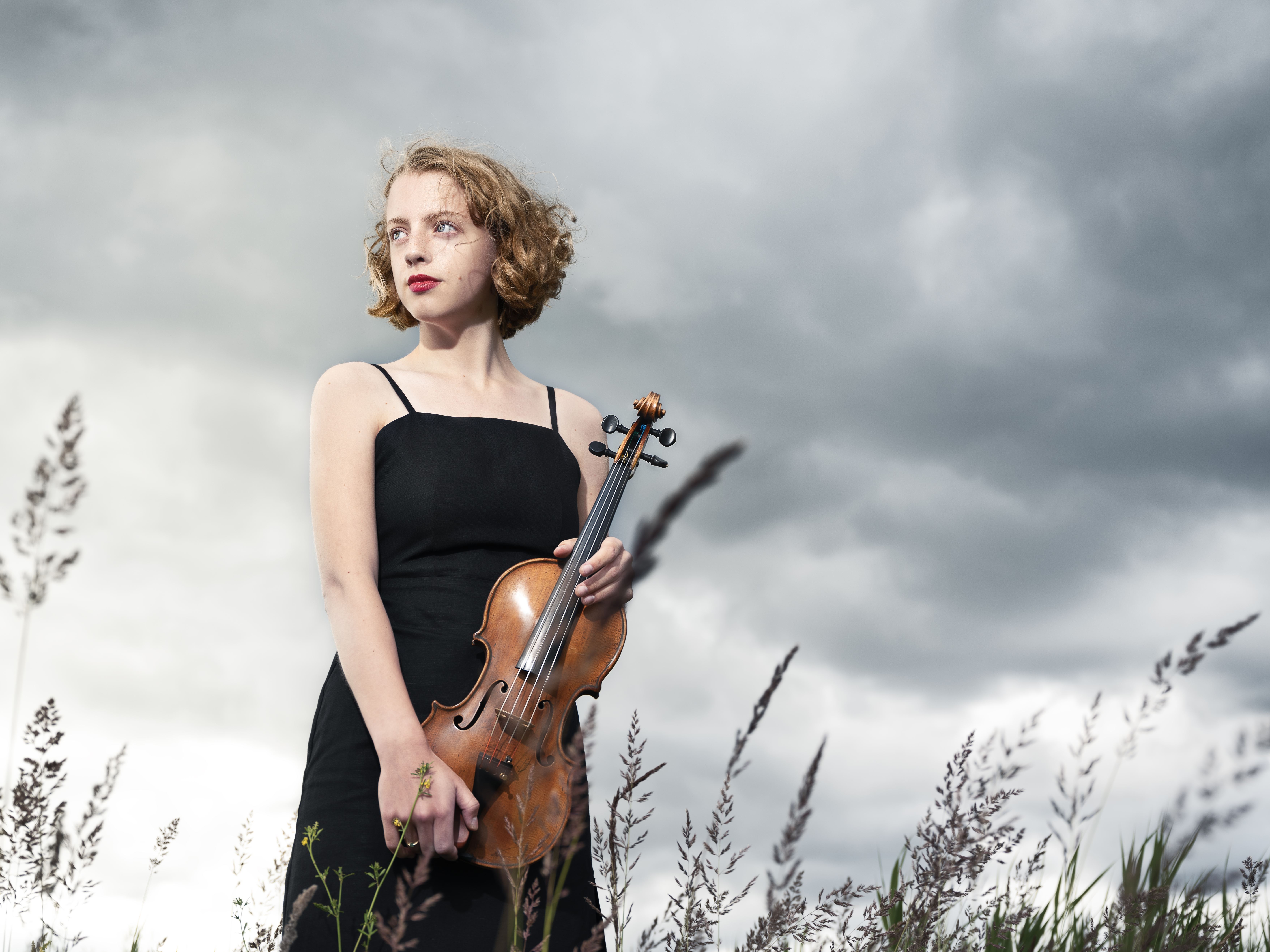 Solistprisvinnaren Alva Holm står ute på en äng med violinen i handen