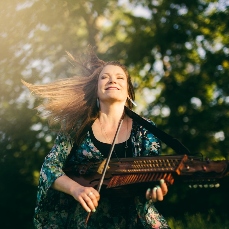 Nyckelharpisten Emilia Amper står ute i solen och spelar på sin nyckelharpa
