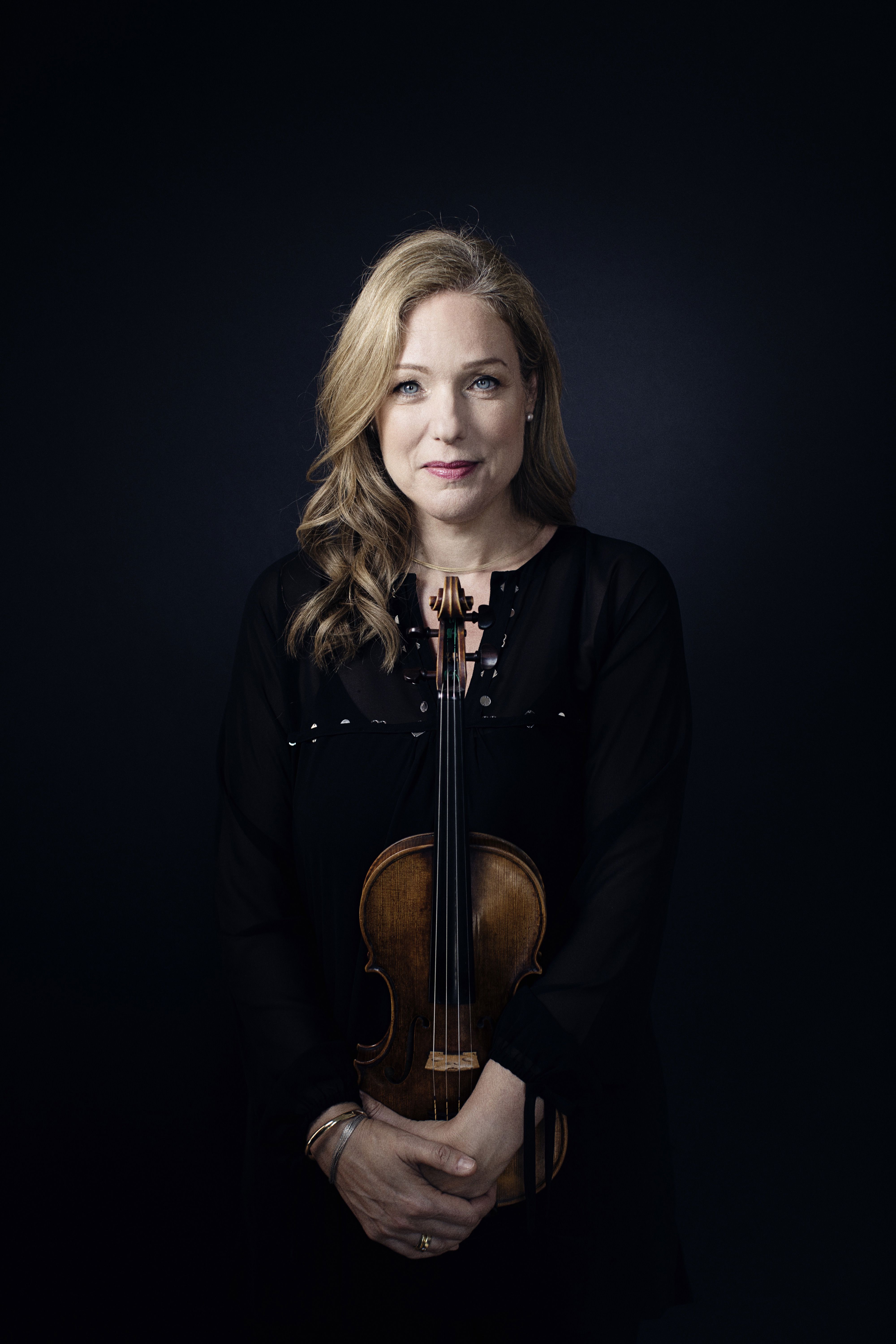 Porträttbild på violinisten Isabelle van Keulen hållandes i en violin. Bakgrunden är mörkblå och svart.