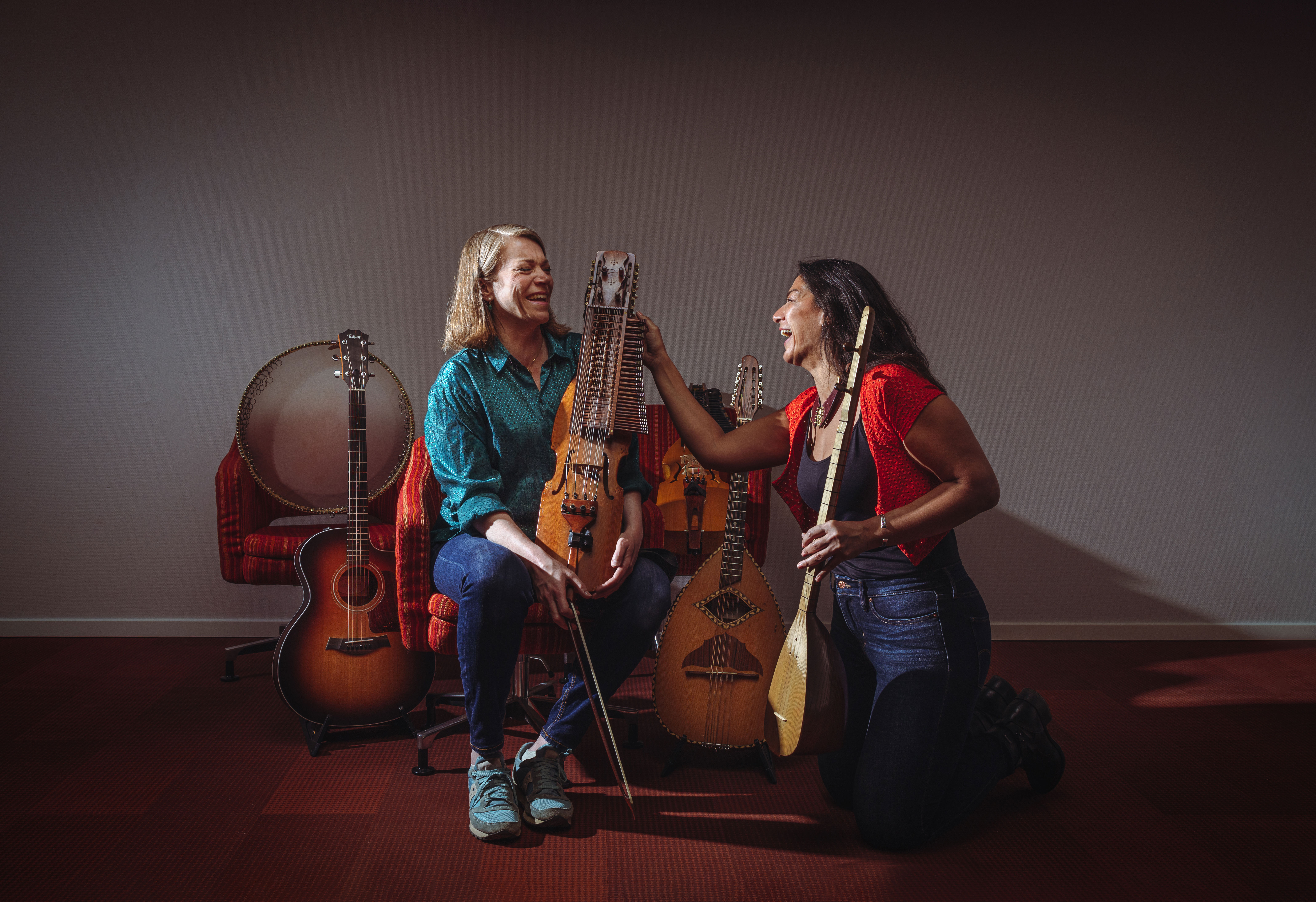 Multimusikerna Emilia Amper och Nadin Al Khalid sitter på ett trägolv. Runt om dem står en massa olika musikinstrument. Ansiktsuttrycken utstrålar glädje.