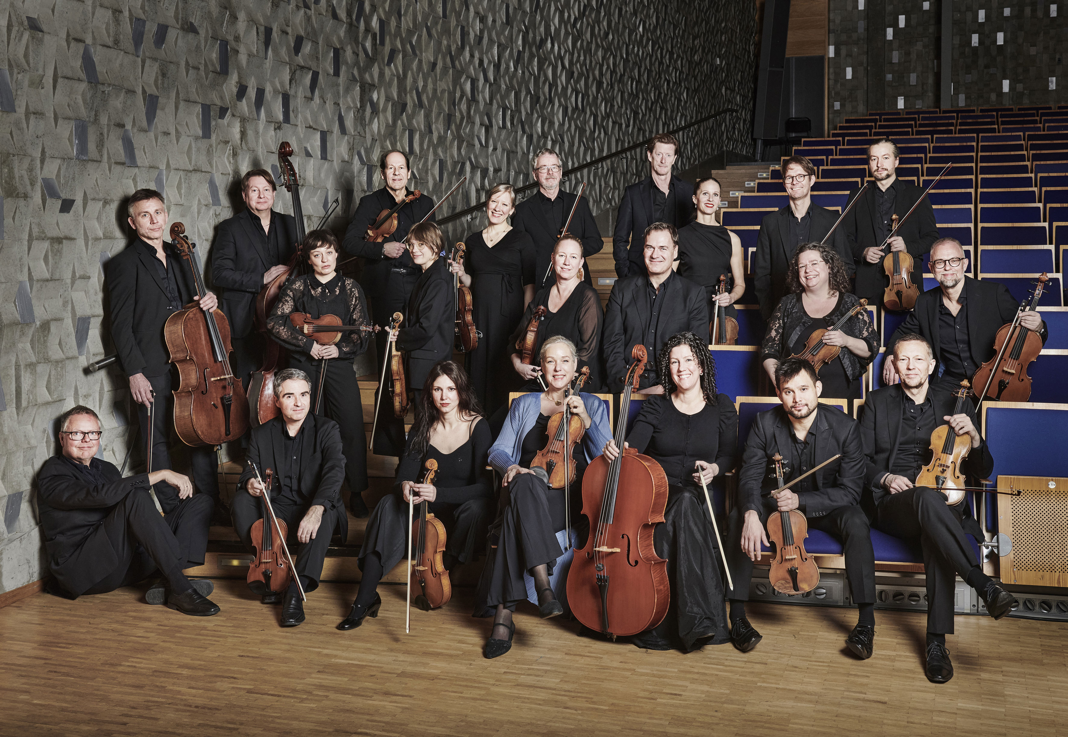 Ensemblebild på musikerna i Norrbottens Kammarorkester sittande i stolsraderna i konserthusmiljö.