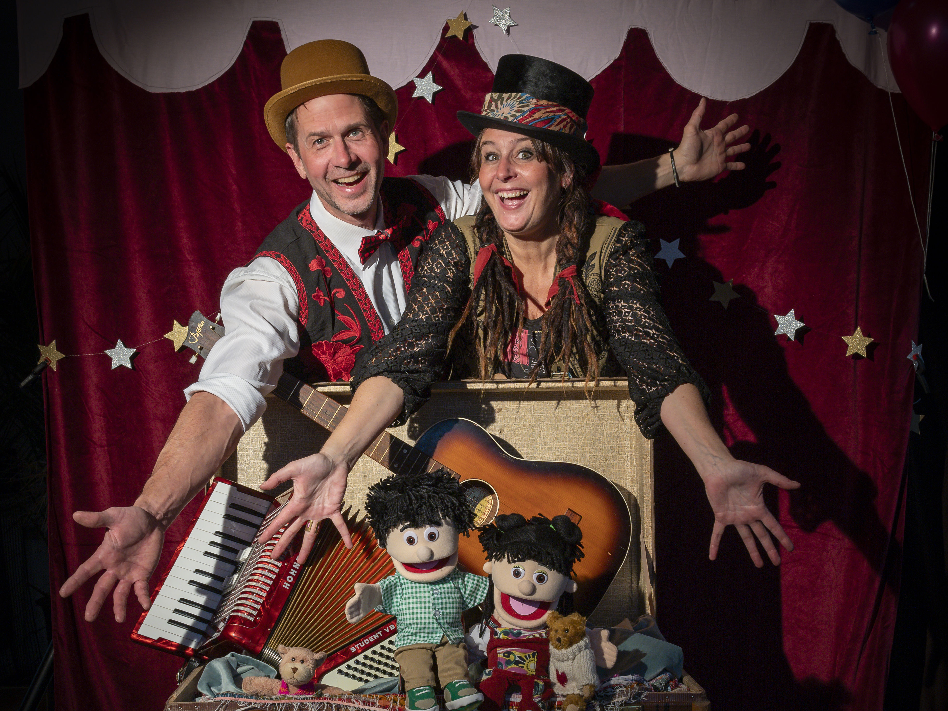 En glad kvinna och man sträcker ut händerna och visar upp en väska med instrument, dockor och en nalle.