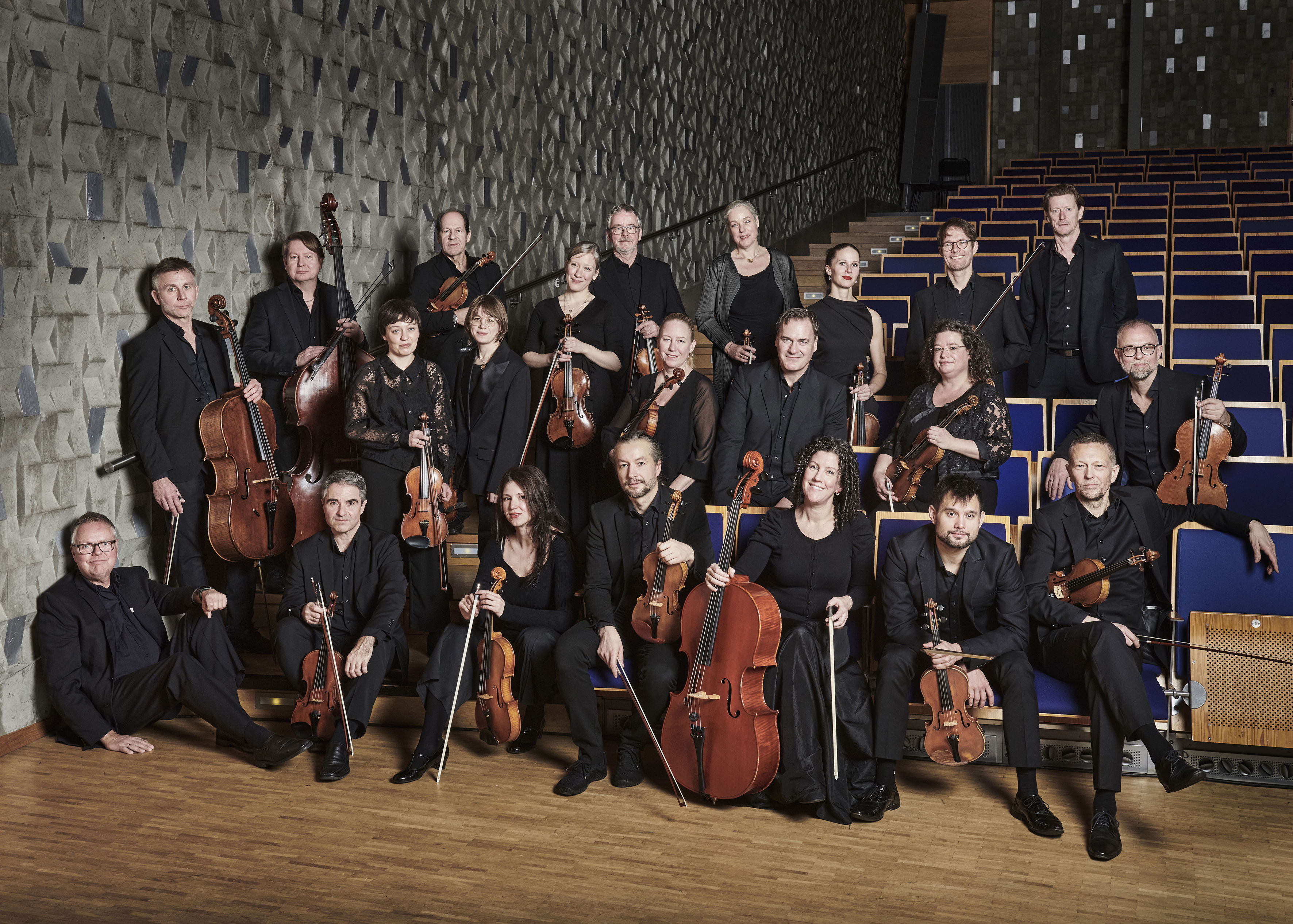 Ensemblebild på musikerna i Norrbottens Kammarorkester sittande i stolsraderna i konserthusmiljö.