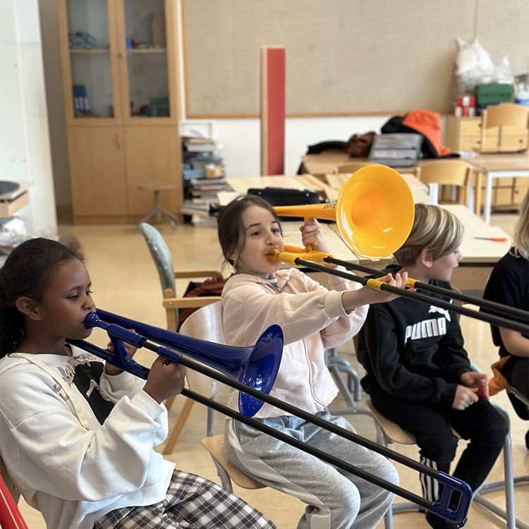 Skolelever sitter på stolar i ett klassrum och spelar på färgglada tromboner