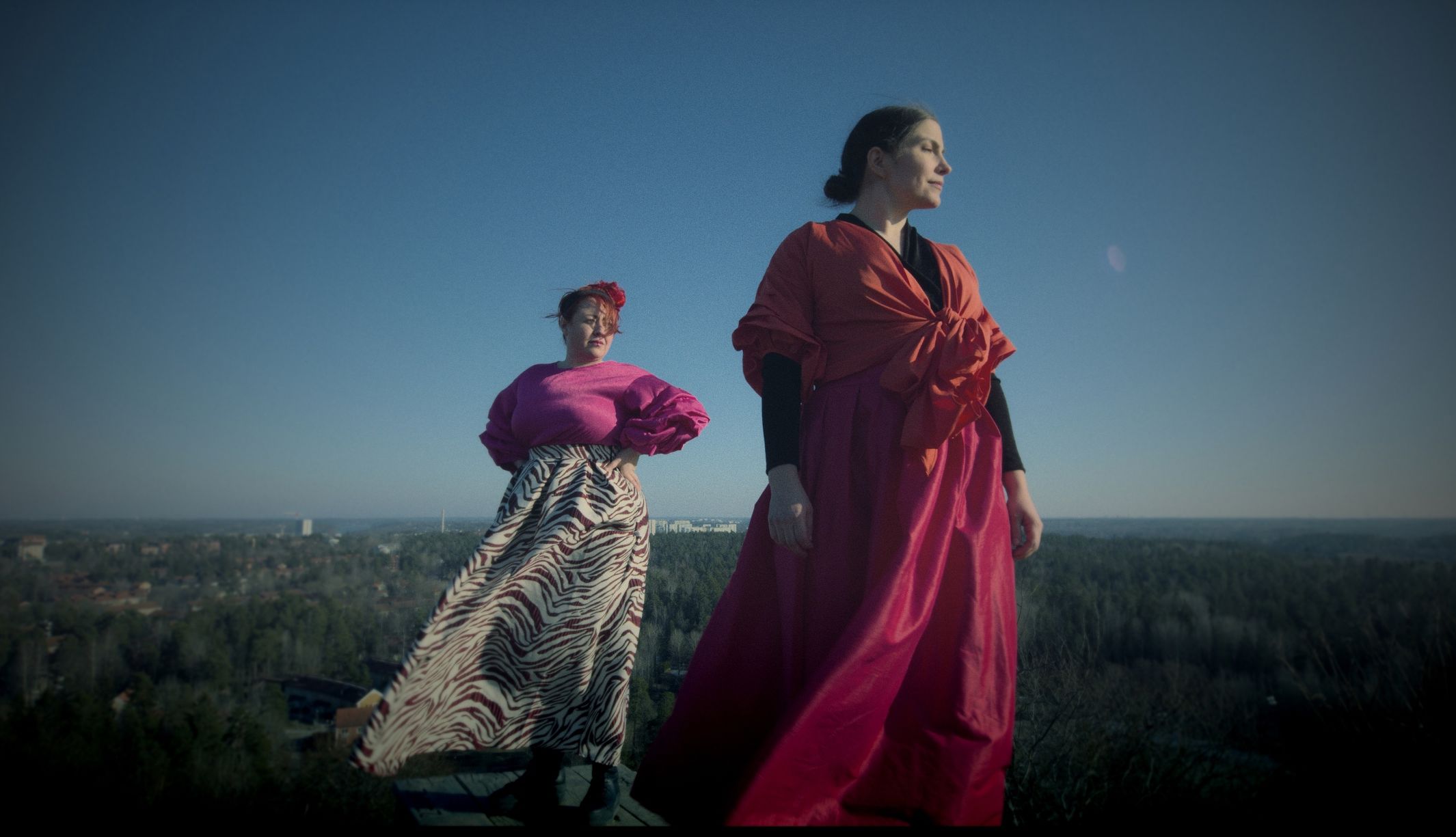 Artister och låtskrivarna Vera Vinter och Hanna Ekström står uppe på ett berg med solen i ansiktet. Vinden tar tag i de lössittande kläderna. 