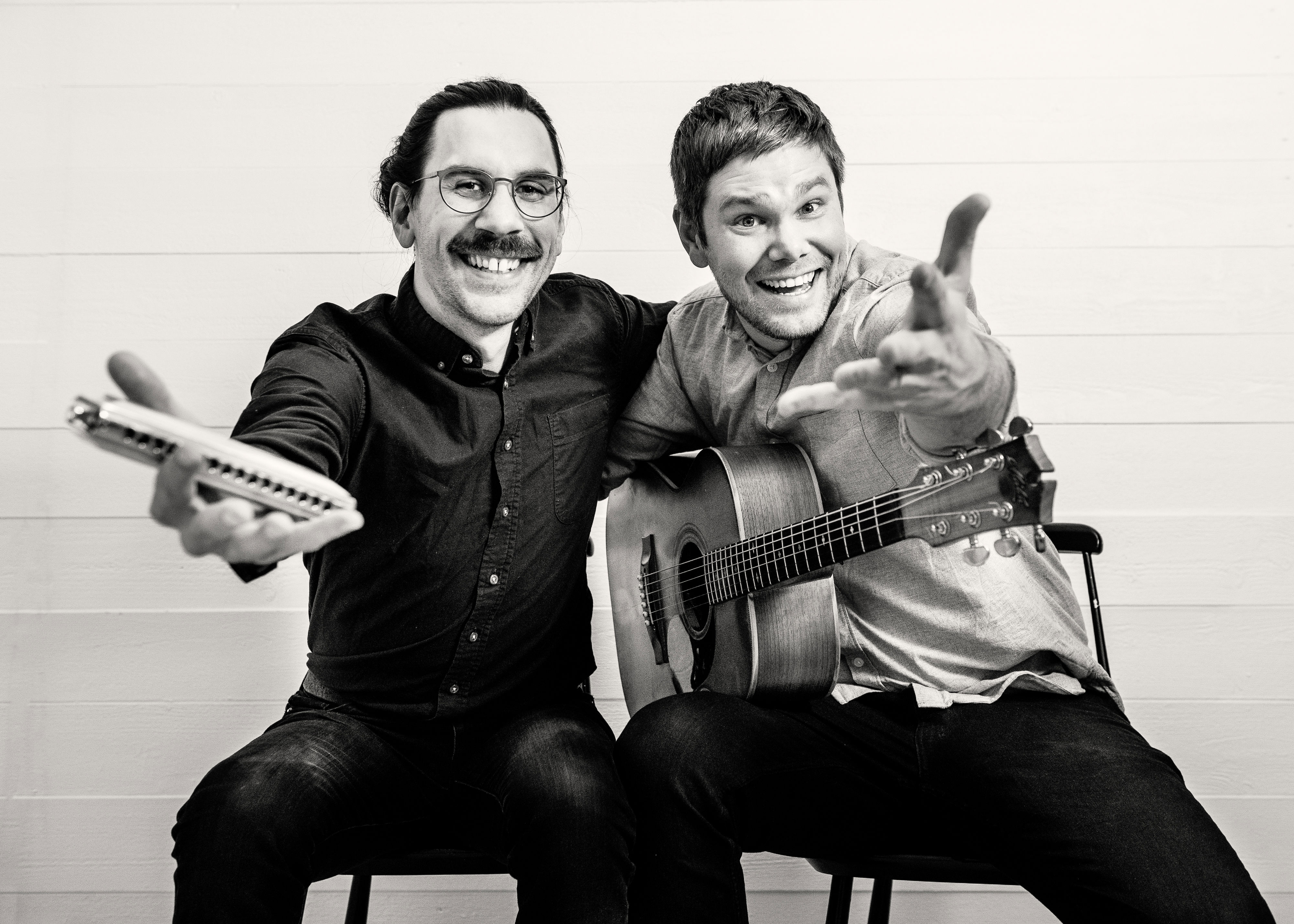 Musikerna Filip och Emil sitter mot en ljus bakgrund. En håller i ett munspel och den andra i en gitarr.